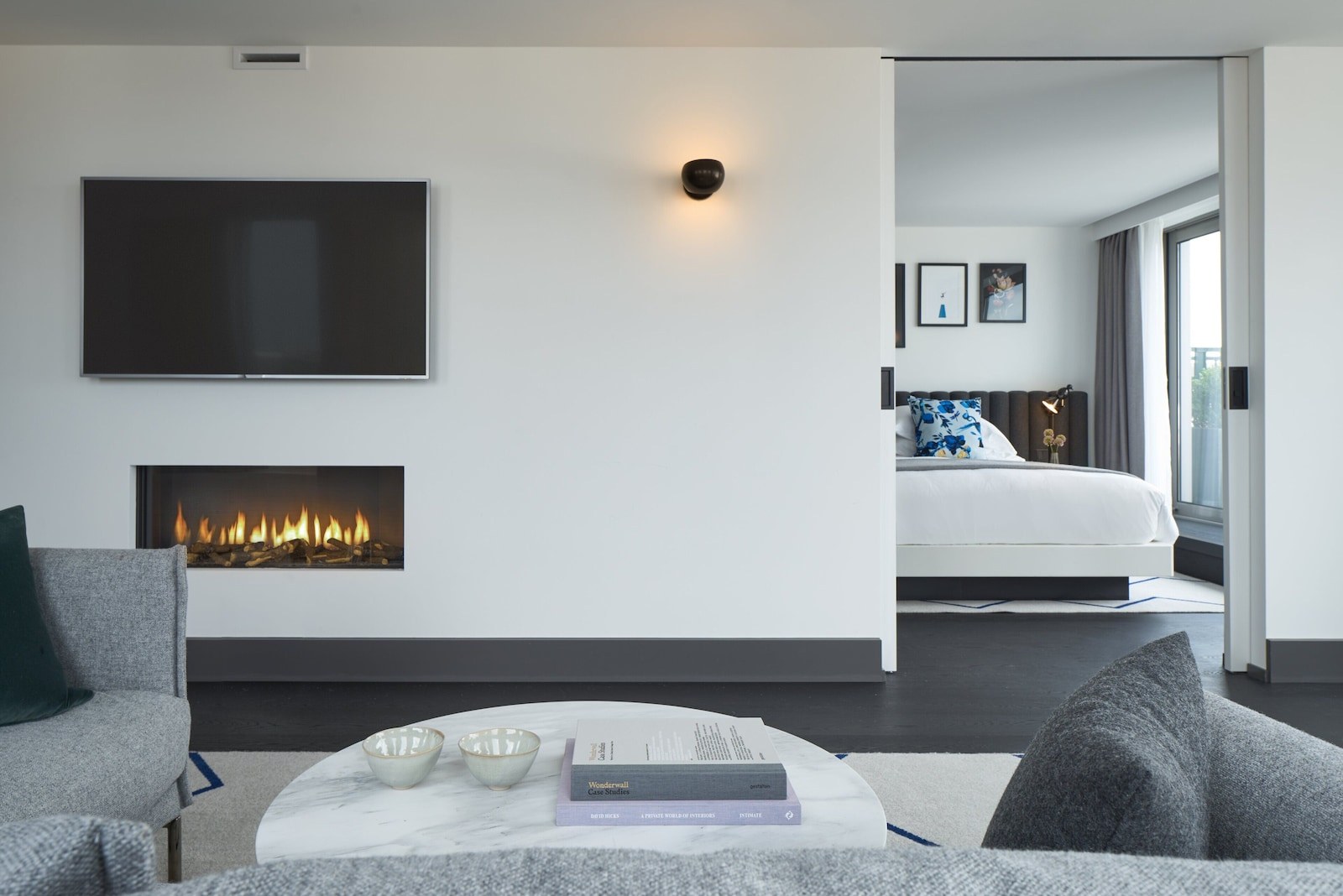 A modern hotel room with a flat-screen TV, a fireplace, a bed with a headboard, and a large window. - Kimpton De Witt Amsterdam by IHG (Amsterdam)